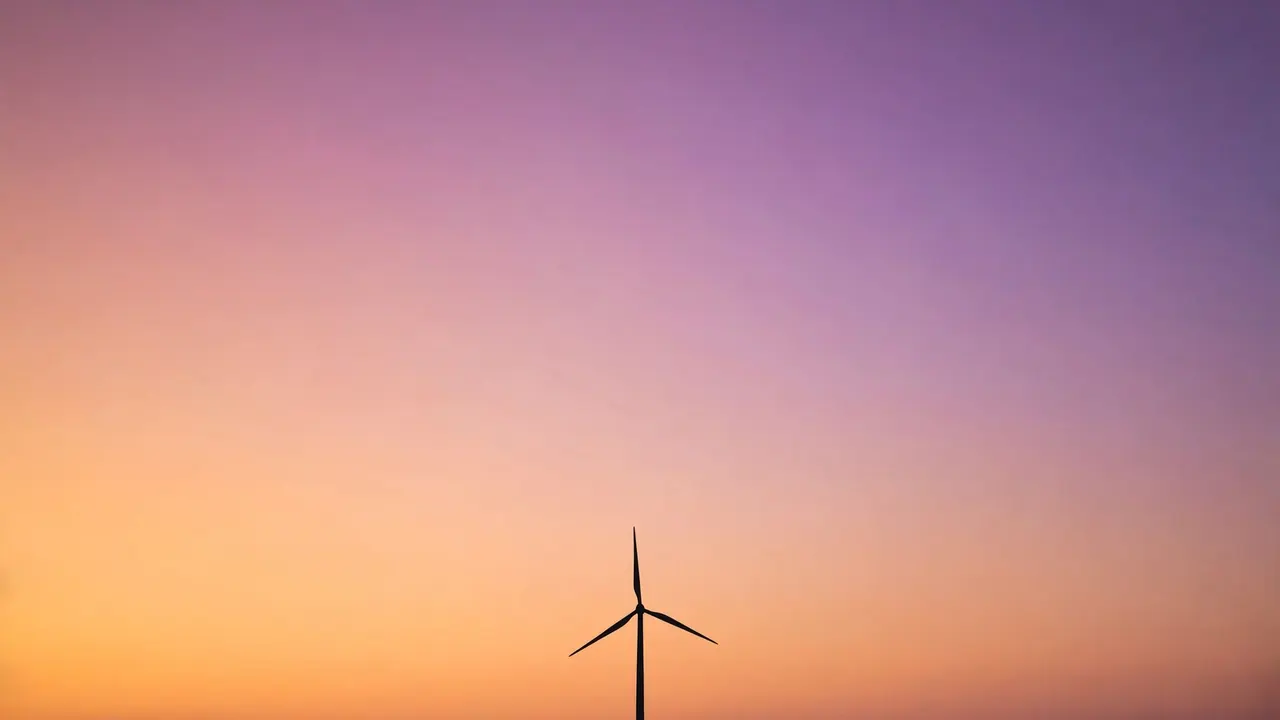 A lone wind turbine silhouetted against a gradient sunset sky.