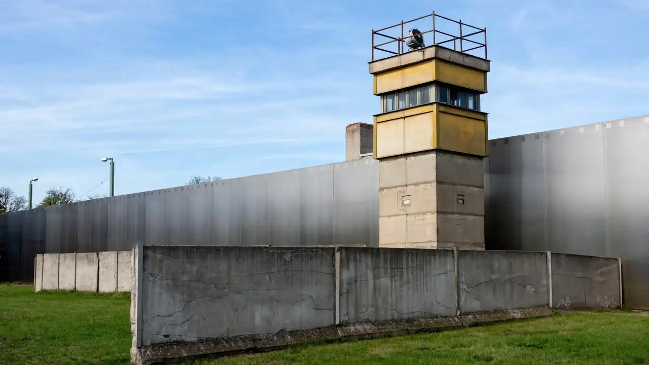 The preserved Berlin Wall memorial at Bernauer Strasse with a watchtower, green lawn and clear sky