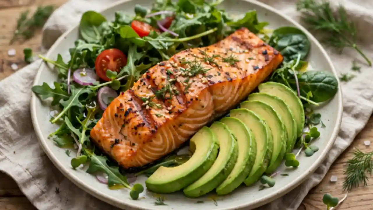 A plate of grilled salmon with avocado slices and leafy greens
